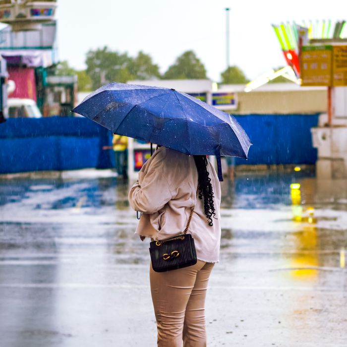 A woman with a blue umbrella stands on a rainy urban street, reflecting vibrant lights.