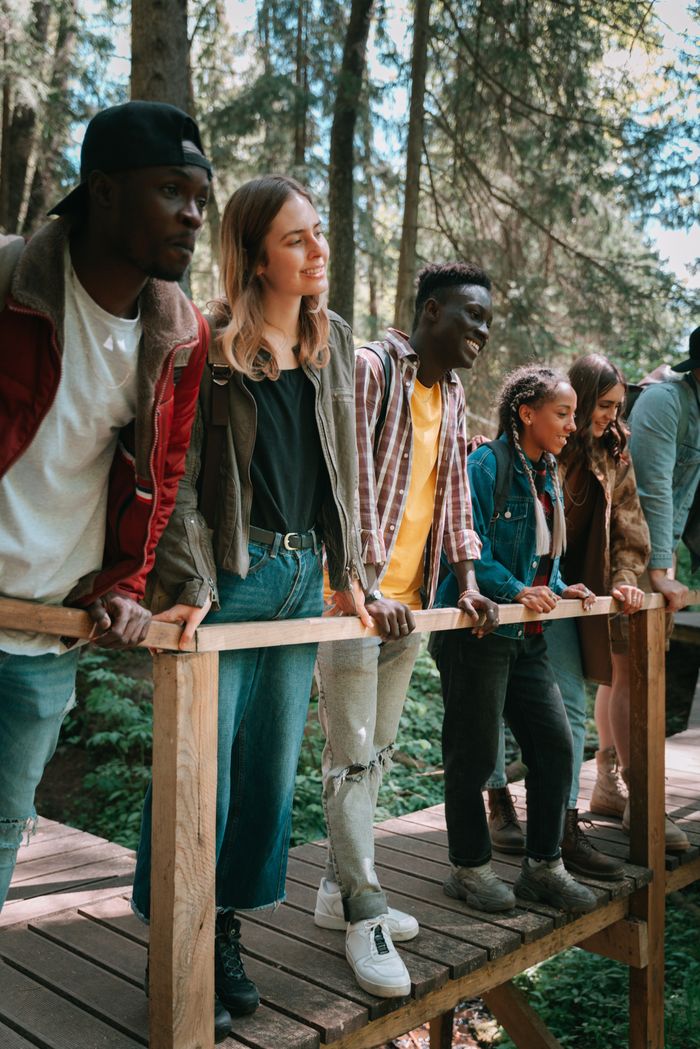 A diverse group of friends enjoying a hike on a wooden bridge in a forest setting.